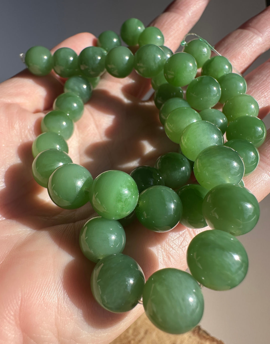 Intimate close up of green 10mm jade beads on string being held by fingers