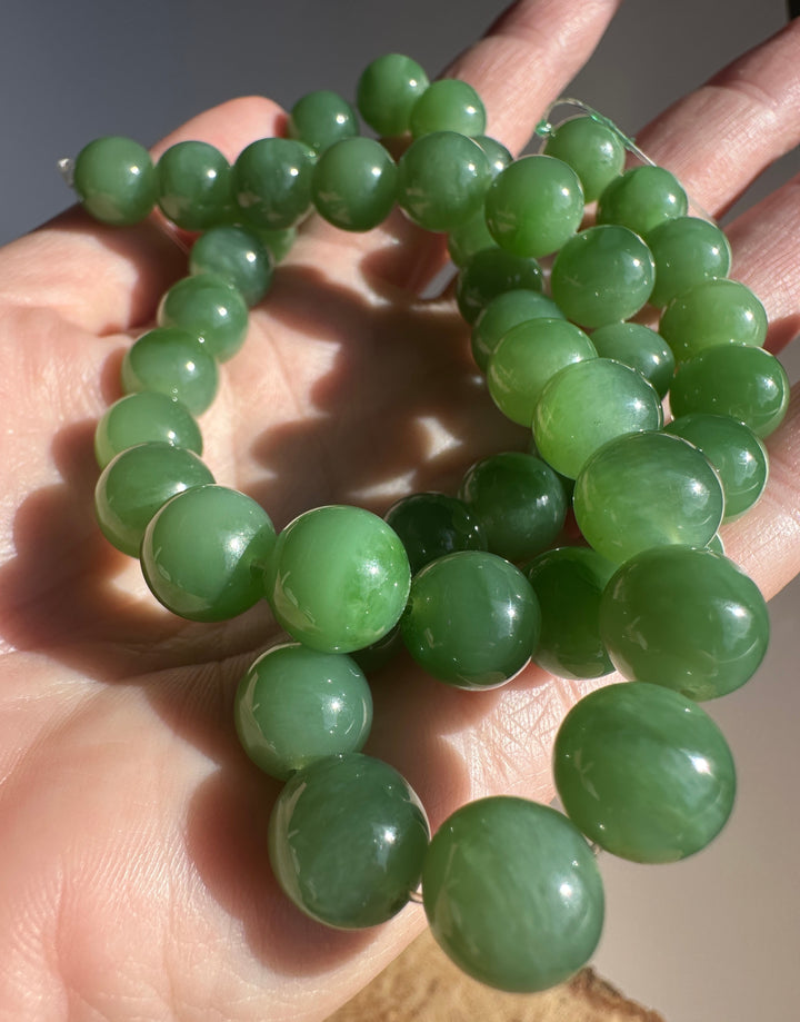 Intimate close up of green 10mm jade beads on string being held by fingers