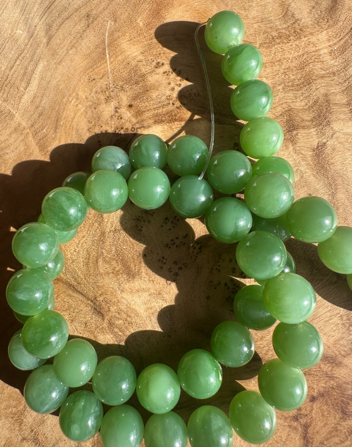 Unstrung 10mm green Siberian jade beads laid out along a curved strand on a wooden surface