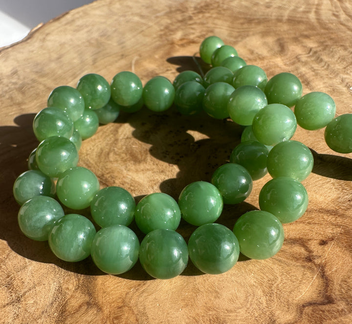 Unstrung 10mm green Siberian jade beads with a visible cord running through the row on a wooden surface