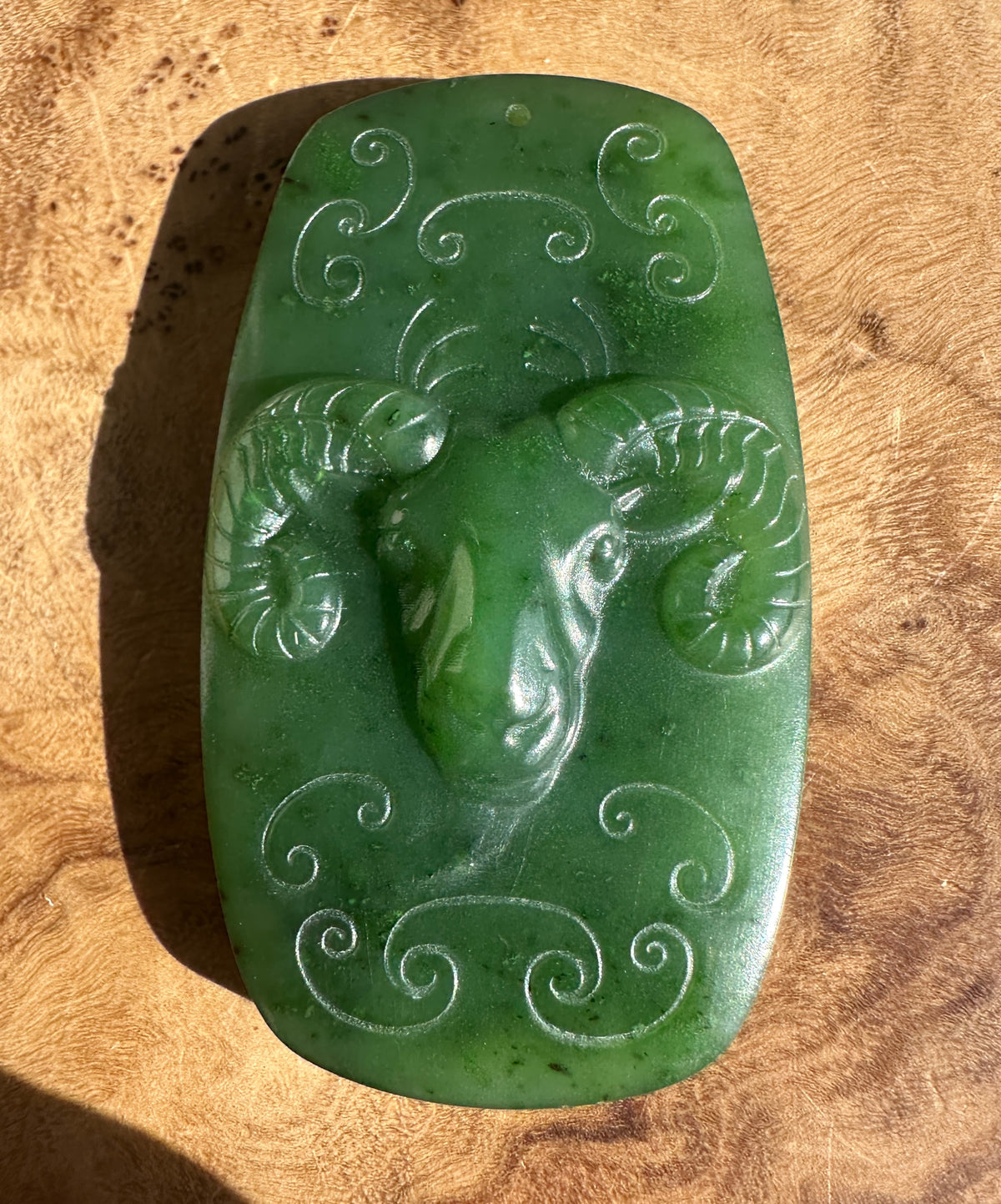 Green jade Ram Pendant with swirling scroll engravings across the surface.