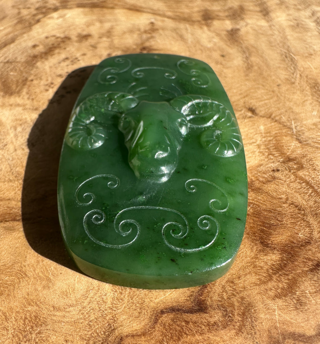 Green jade Ram Pendant viewed from an angle, showing curled scroll patterns.