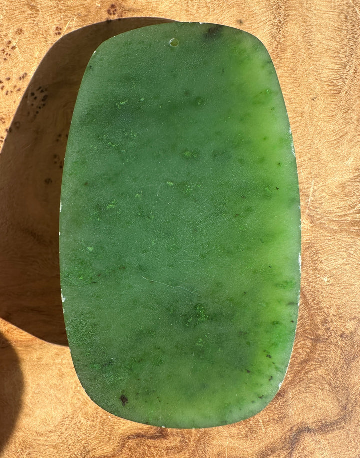 Close up of the lower area of the green jade ram pendant with engraved scrolls and a smooth surface.