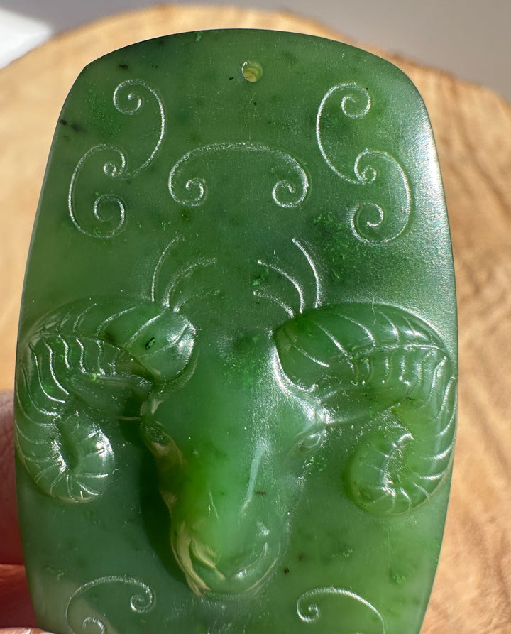 Top corner view of a green jade ram pendant showing a string hole and swirling engravings.