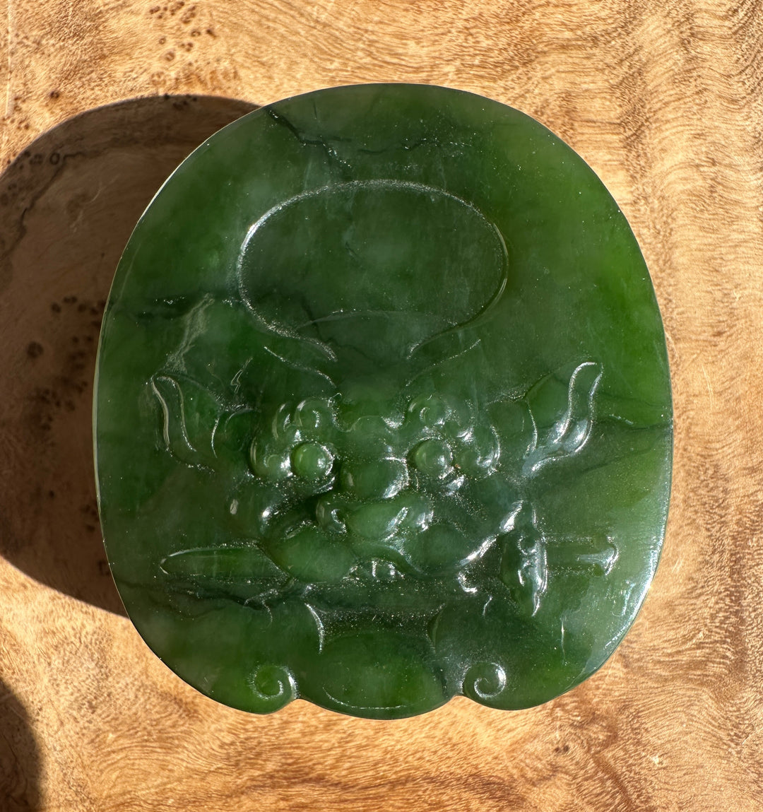 Close up of a dark green jade belt buckle with etched decorative lines.