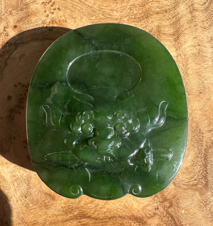 Close up of a dark green jade belt buckle with etched decorative lines.