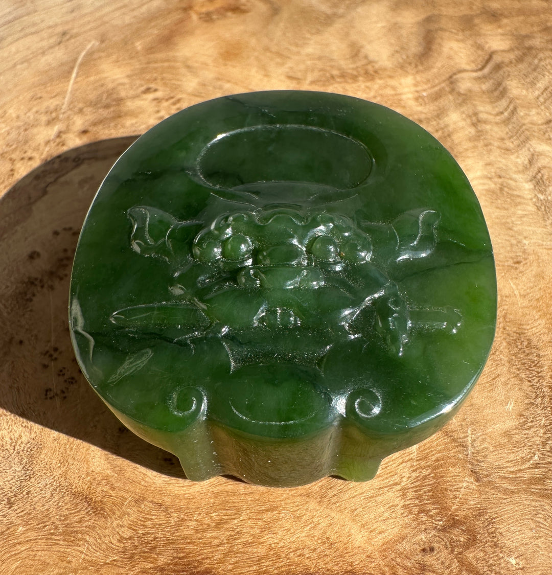 Front view of a polished green jade belt buckle with a carved design along the bottom edge.
