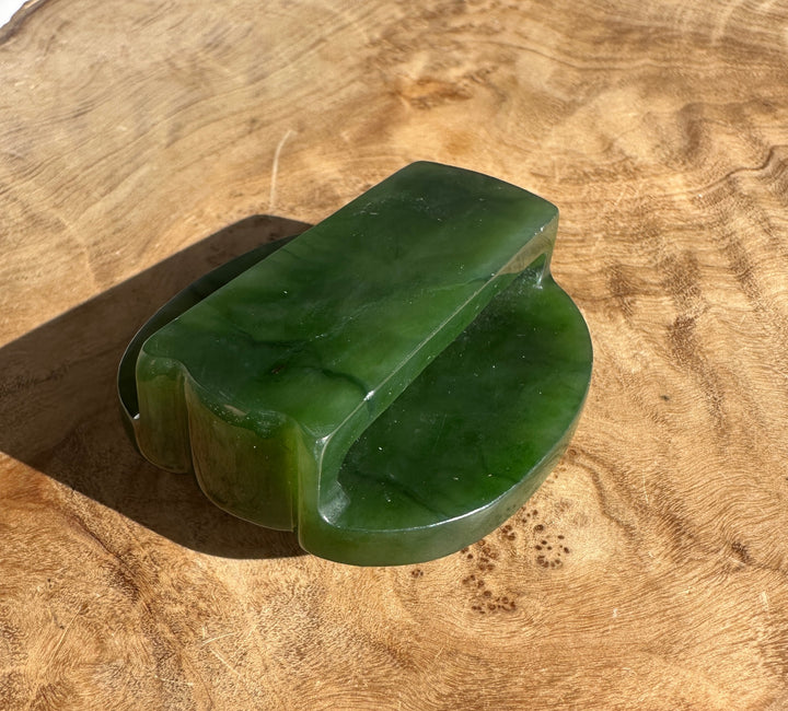 Green jade belt buckle resting on a wooden surface showing its curved edge.