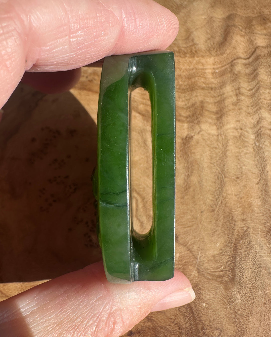 Close up of a green jade belt buckle edge with a central slot held between fingers.