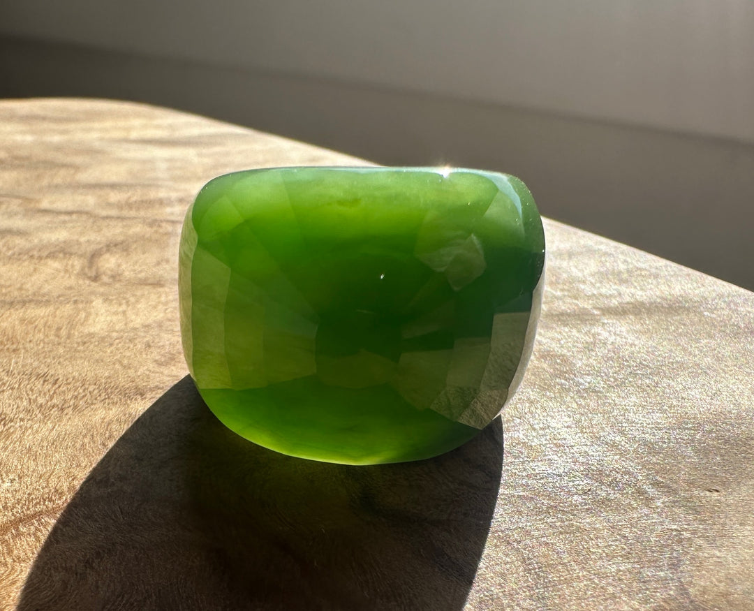 Angle view of a faceted green jade ring catching light against a tan textured surface