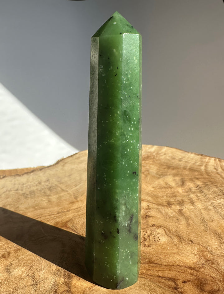 Tall green Canadian Ogden jade obelisk with a pointed top resting on a wooden surface