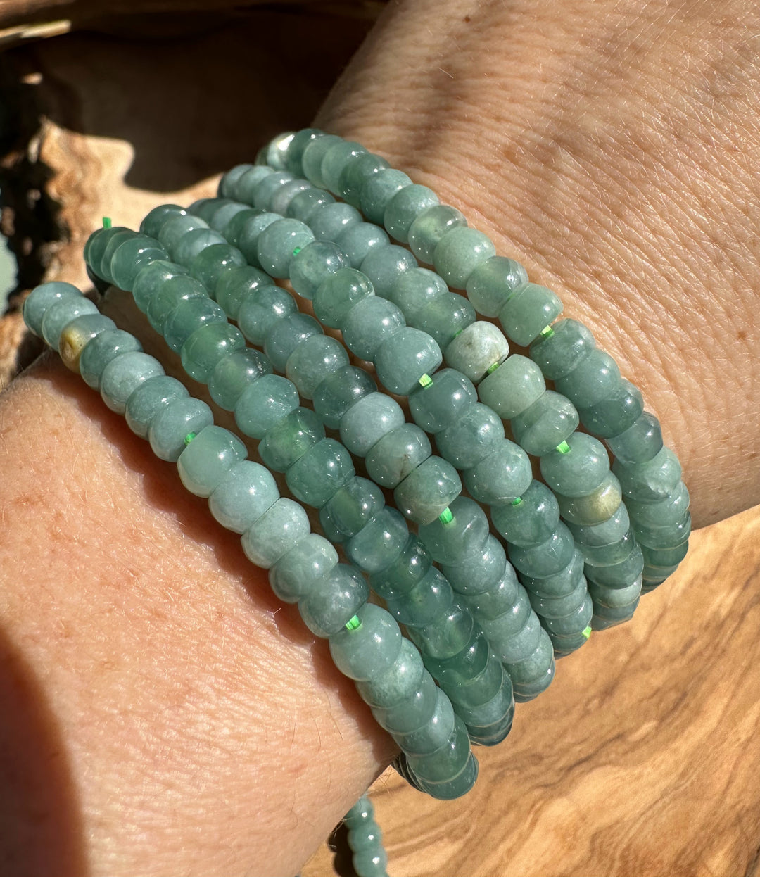 Multiple Guatemalan jadeite rondelle bead bracelets stacked around a wrist in bright sunlight