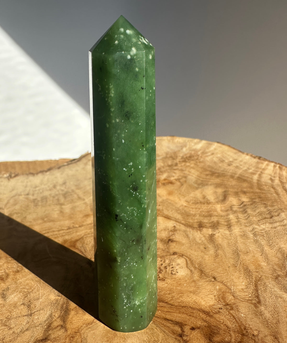 Canadian Ogden Jade 4.25 inch tower crystal standing upright on a wooden surface with a gray background.