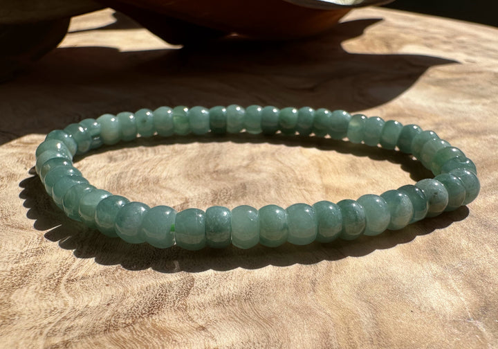 Single jadeite rondelle bead bracelet placed on a wooden surface in bright sunlight