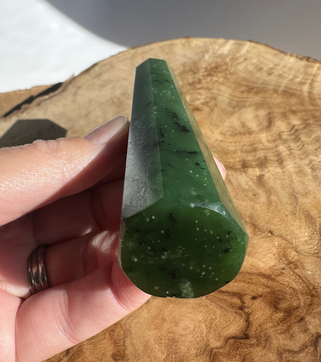 Close up of a green jade obelisk held between fingers against a brown textured background