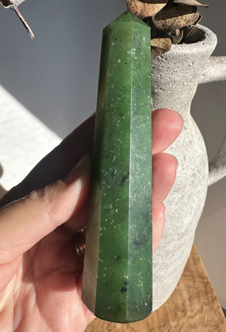 Green jade tower held in hand with a rustic pot and dried plant in the background