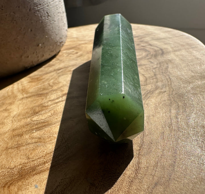 Green jade 4.25 inch obelisk standing upright on a wooden table with a pottery pot nearby