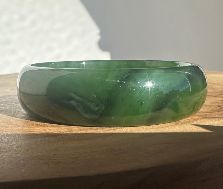A polished green jade bangle bracelet resting on a wooden surface with a neutral background.