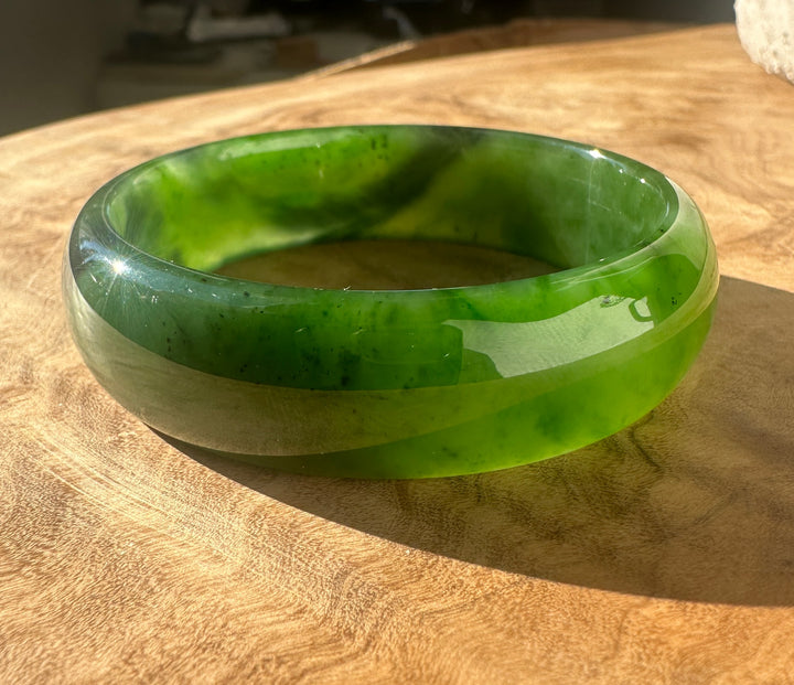 A polished green jade bangle bracelet resting on a wooden surface.