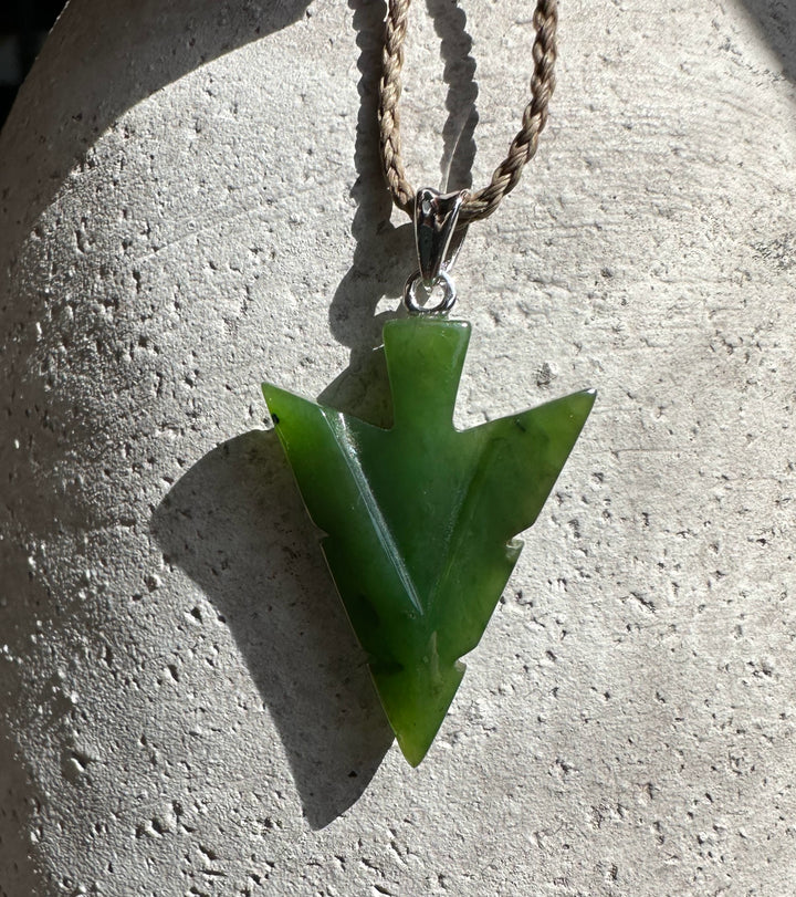 Canadian Jade Arrow Pendant on a tan braided cord necklace against a light concrete surface