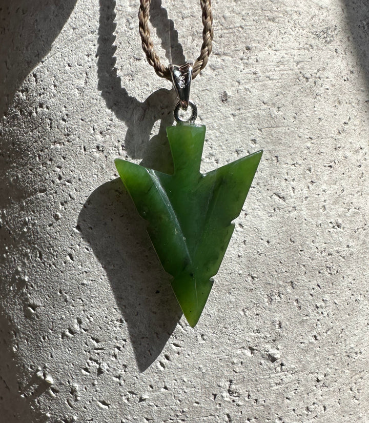 Canadian Jade Arrow Pendant on a tan braided cord with a 925 stamped bail against rough concrete