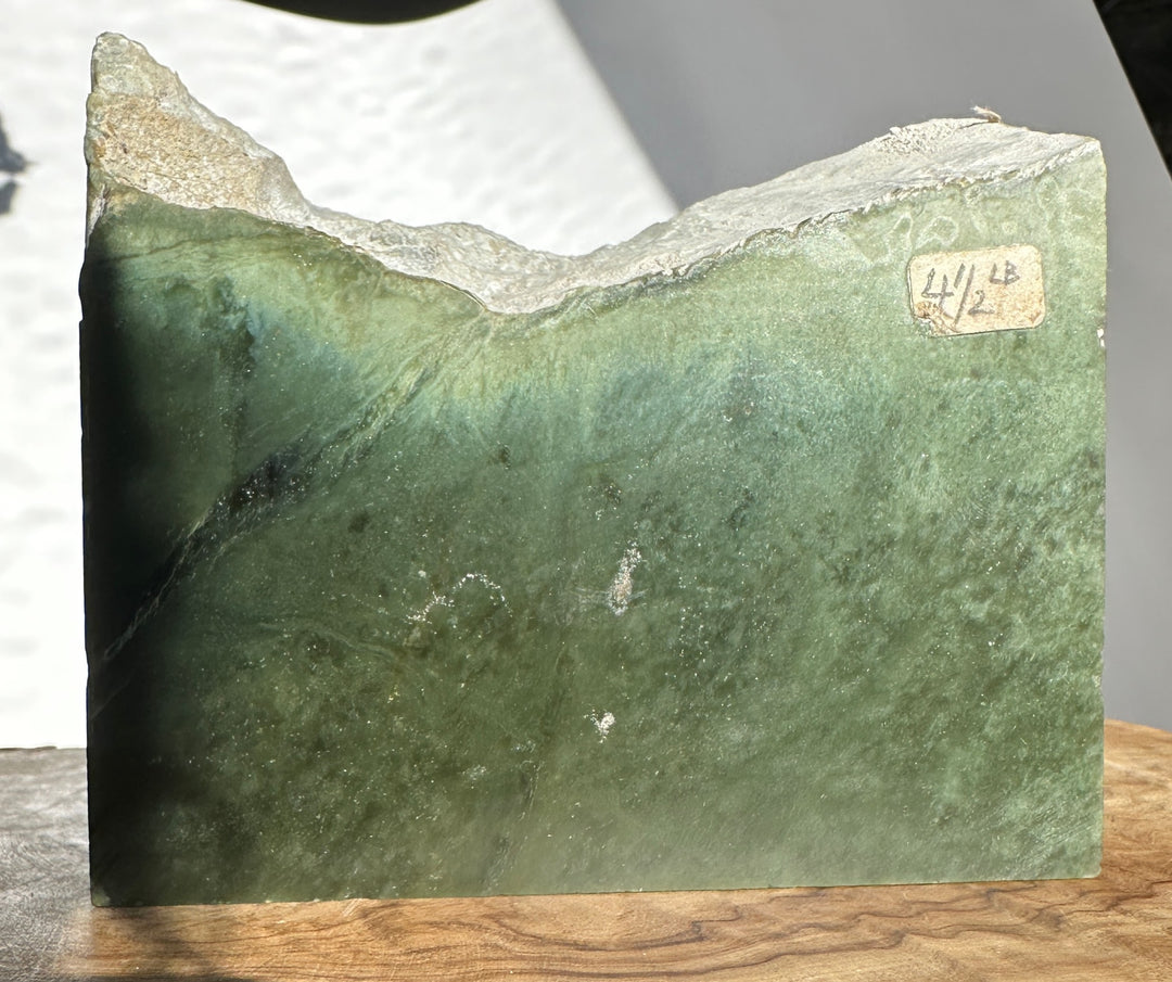 Rough Wyoming jade slab with green body and a light tan cap and a small weight label on the side