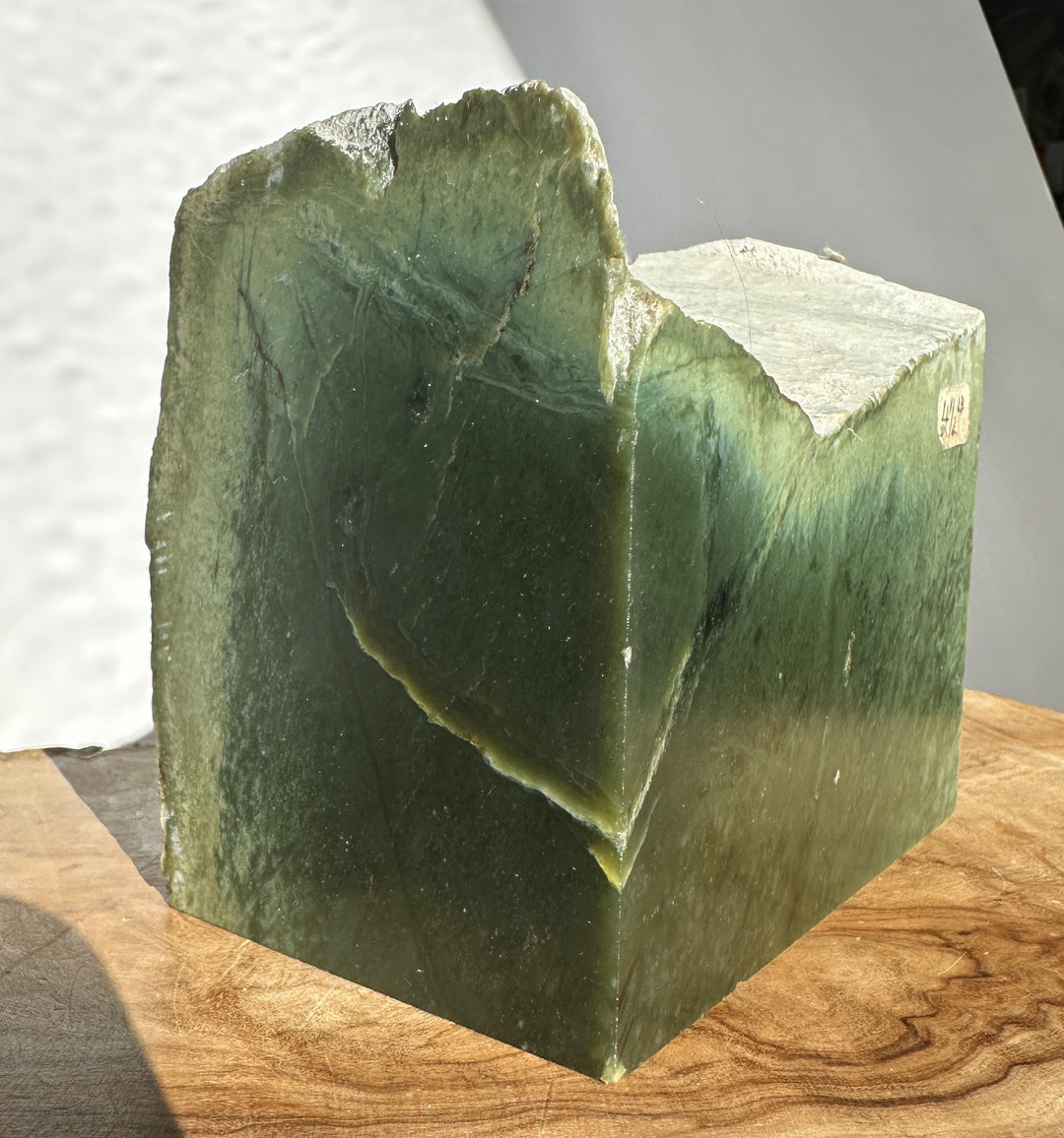 Another angle of Wyoming rough jade showing green surface and pale edges with a small label on the face