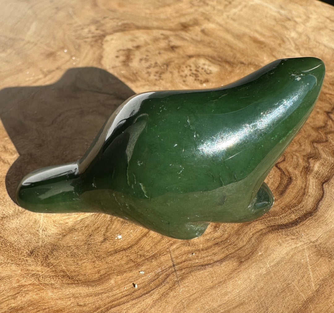 Green nephrite jade beaver carving with a polished surface resting on wood