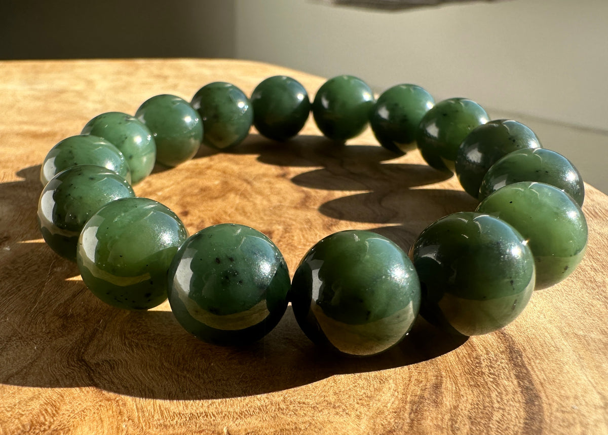 Close up of polished green nephrite jade beads forming a bracelet on wood