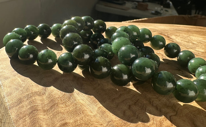 Beads from a 12mm River Canadian nephrite jade bracelet arranged on a wood surface with a glossy finish