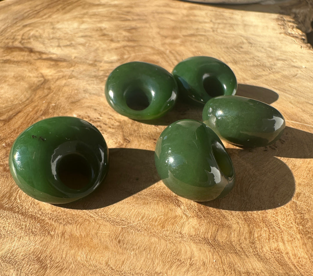 Group of smooth green Cassiar jade beads resting on wood surface under sunlight