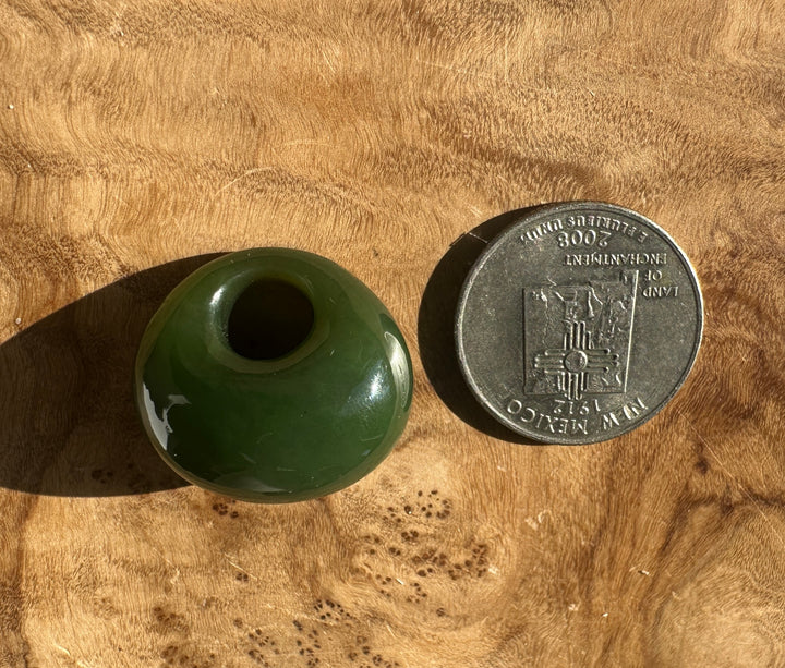 Green Cassiar jade donut shapes on a wooden surface with a coin for scale