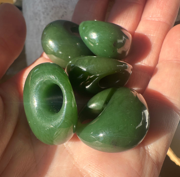 Polished green Cassiar jade donut shaped pieces held in a hand
