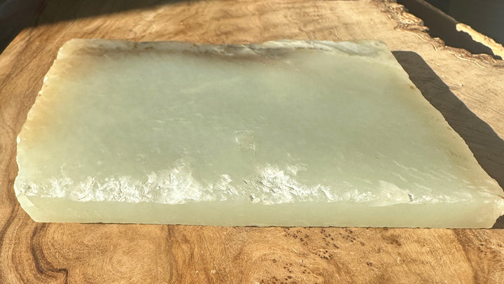 A rectangular pale green translucent stone slab with rough natural edges, placed on a wooden surface.