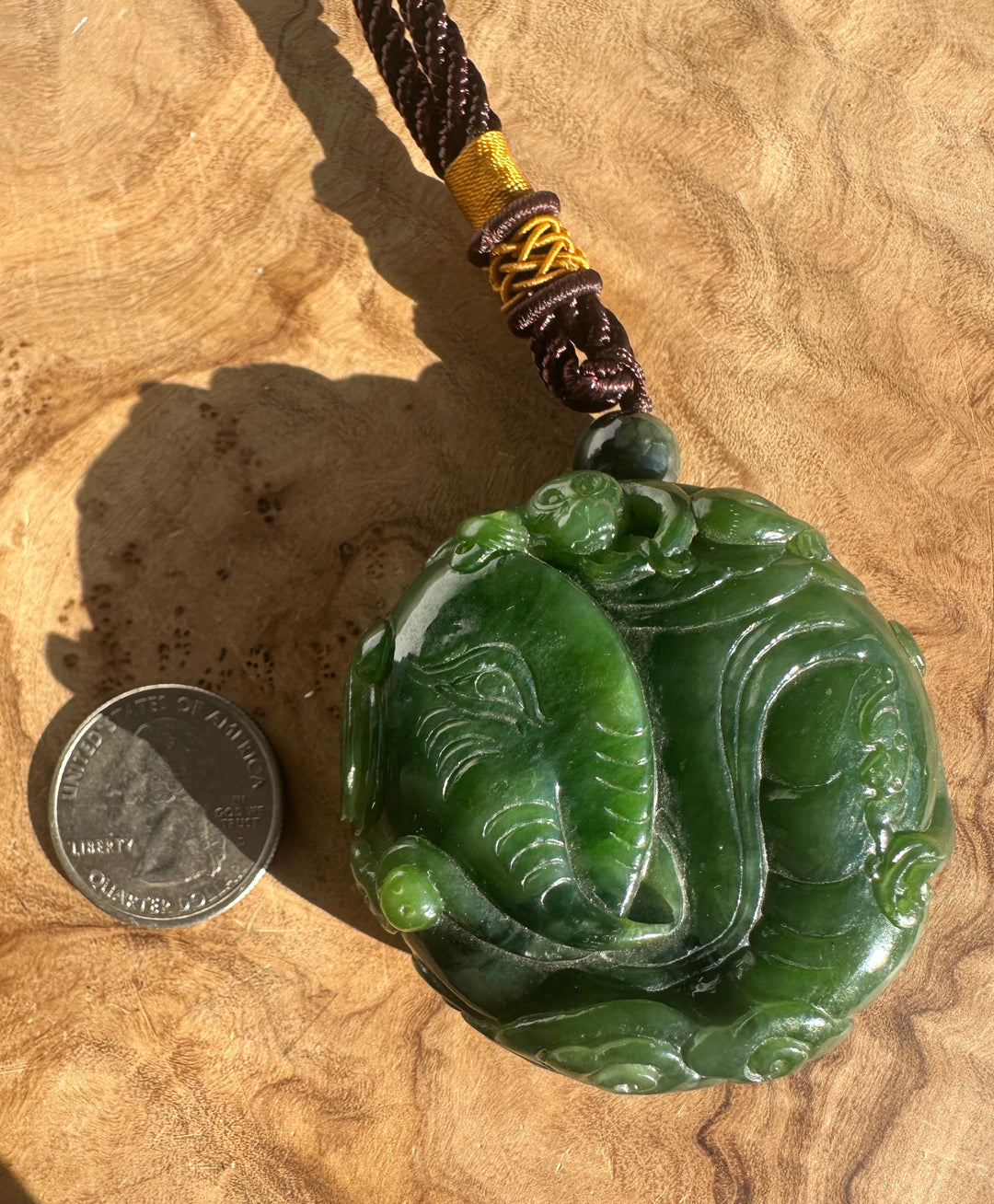 Two coins for scale beside the green jade elephant and monkey pendant with braided brown and yellow cord.