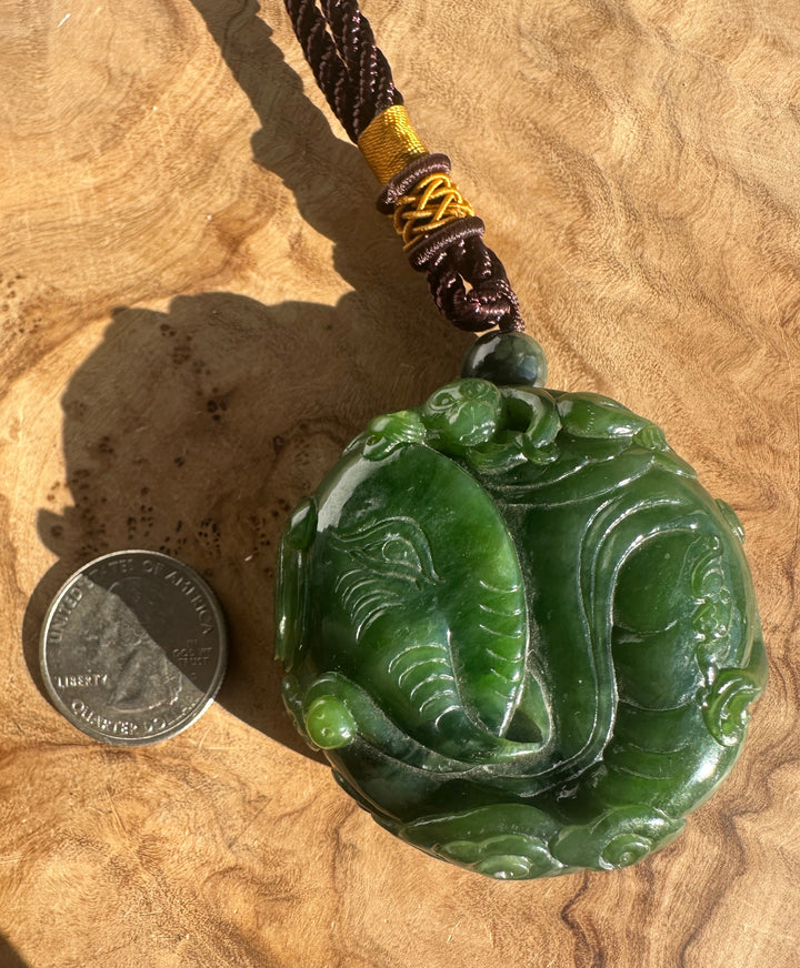 Two coins for scale beside the green jade elephant and monkey pendant with braided brown and yellow cord.