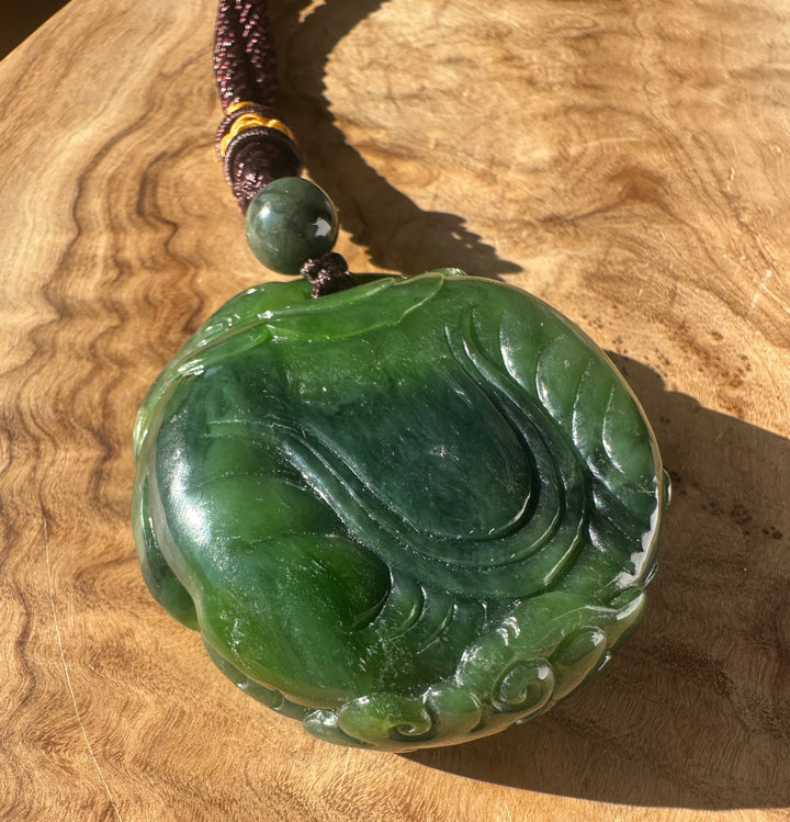 Detail of Nephrite Jade Elephant and Monkey pendant showing a green round bead on a braided cord beside a carved green jade base.