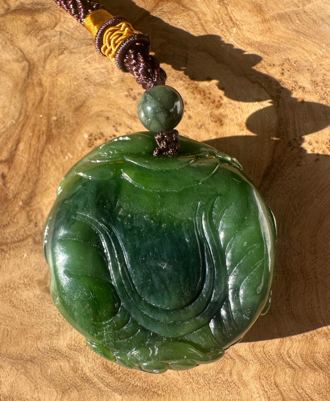 Angled view of Nephrite Jade Elephant and Monkey hand held pendant with a green bead and wrapped brown cord with yellow accents.