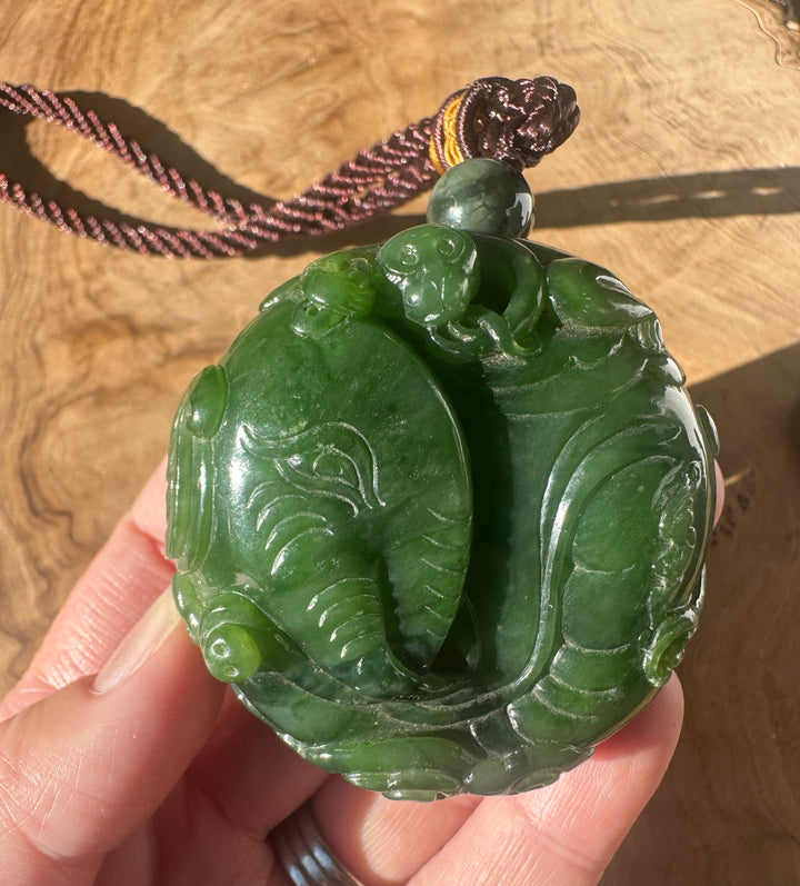 Handheld close up of Nephrite Jade Elephant and Monkey pendant featuring a carved jade base and a suspended green bead.