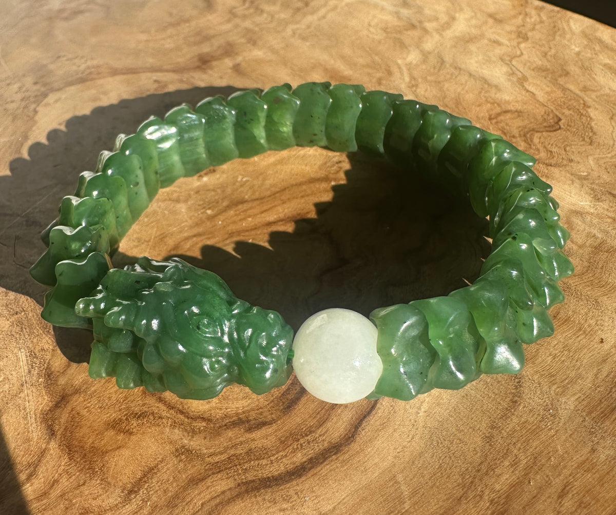 A carved green jade bracelet with a textured, segmented design and a smooth white central bead, displayed on a wooden surface.
