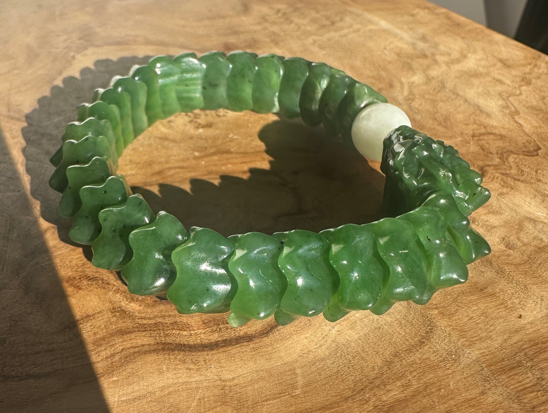 A carved green jade bracelet with a textured, segmented design and a smooth white central bead, displayed on a wooden surface.
