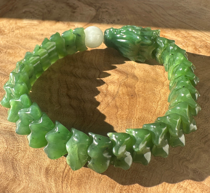 A carved green jade bracelet with a textured, segmented design and a smooth white central bead, displayed on a wooden surface.
