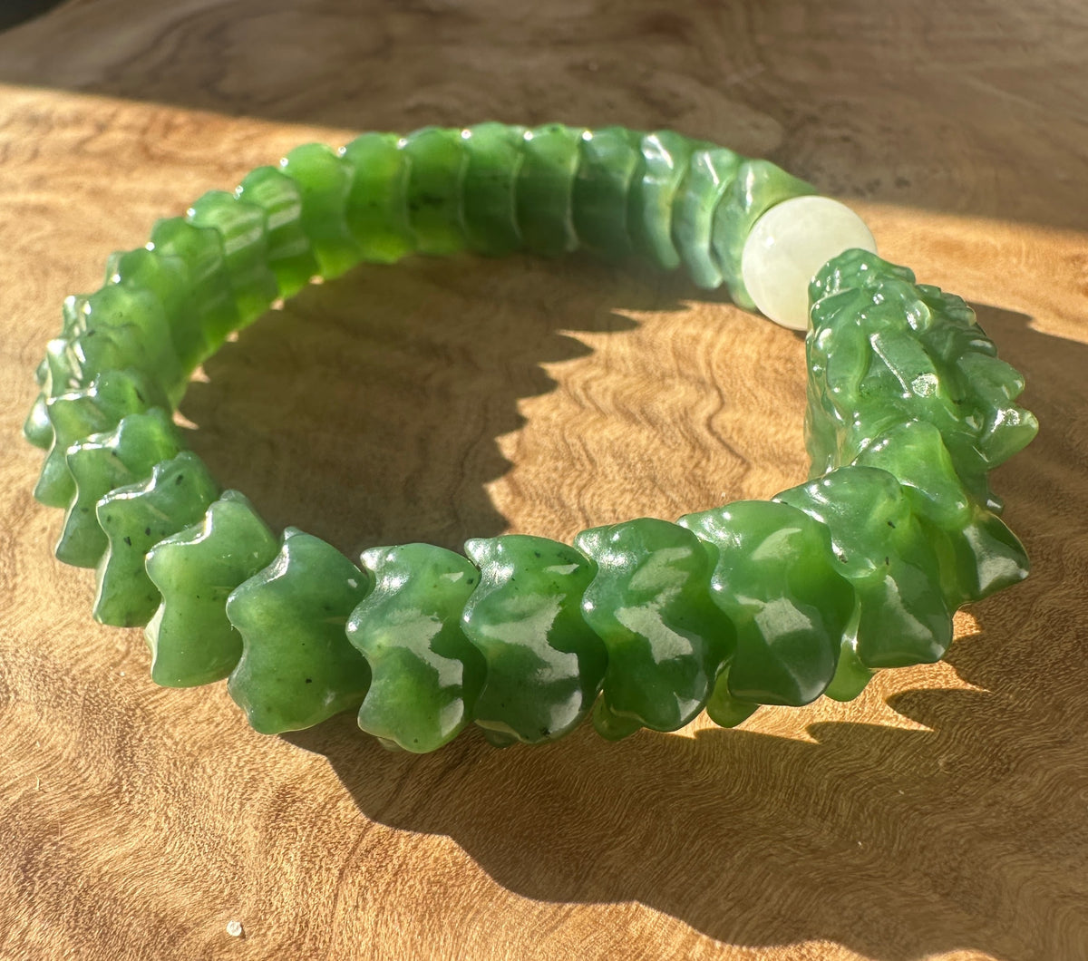 A carved green jade bracelet with a textured, segmented design and a smooth white central bead, displayed on a wooden surface.