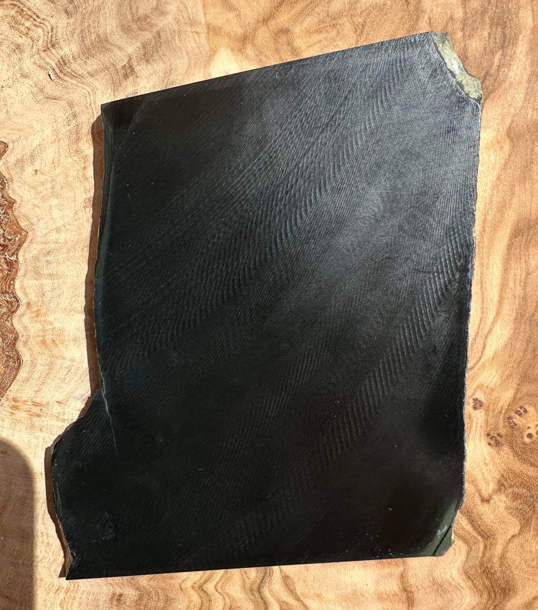 Wyoming Black Jade Slab 210 grams irregular black slab with a chipped corner on a wooden surface