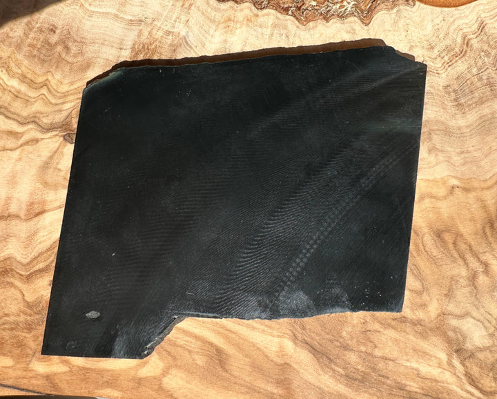 Wyoming Black Jade slab 210 grams on a wooden surface with a small notch at the bottom edge.