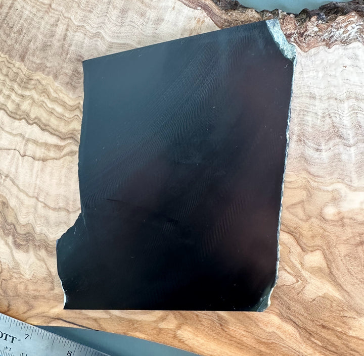 Angled view of Wyoming Black Jade slab 210 grams showing glossy surface and rough edge along the side.