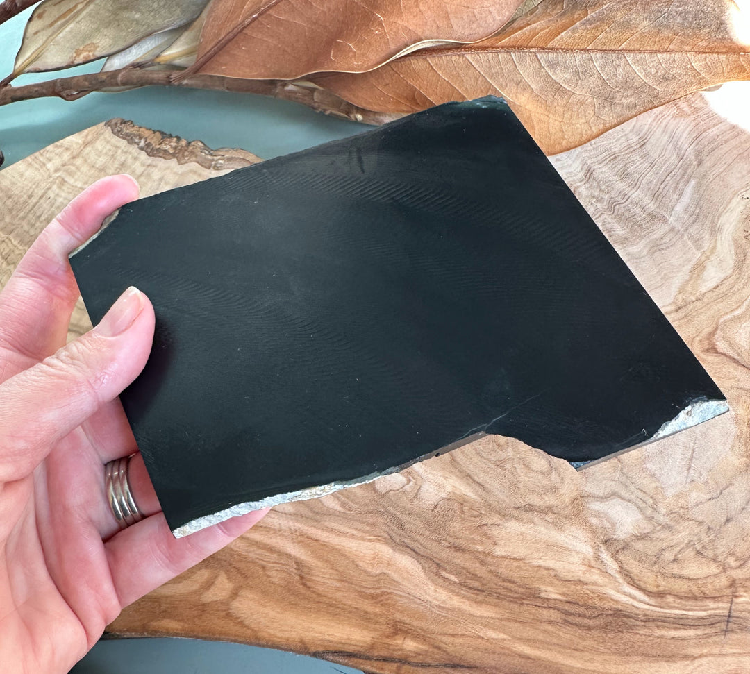 Hand holds a rectangular green jade block with polished surface and natural banding