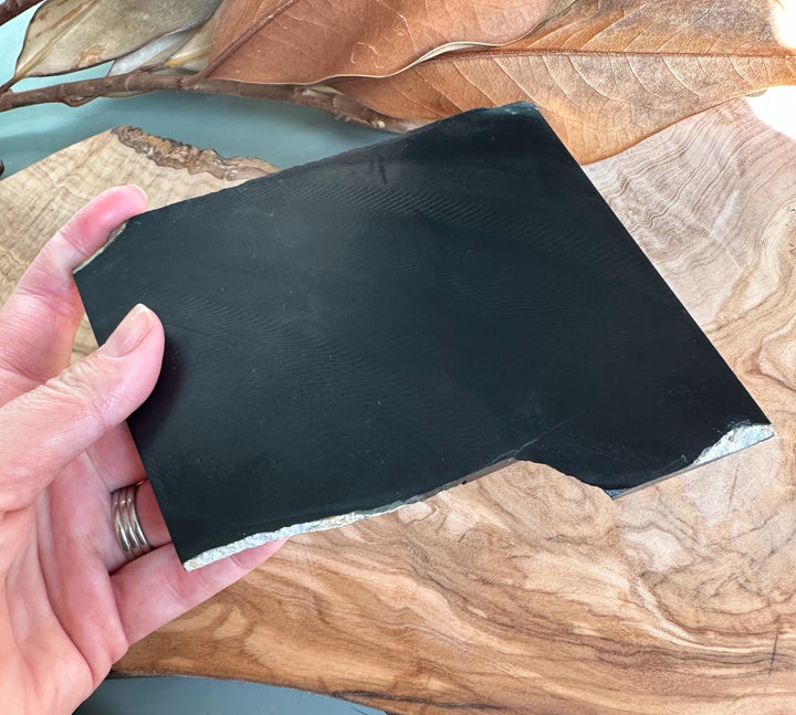 Hand holds a rectangular green jade block with polished surface and natural banding