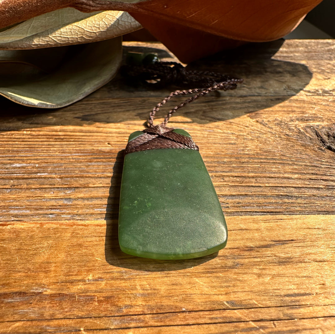 Close up of dark green jade adze pendant wrapped with braided cord on weathered wood