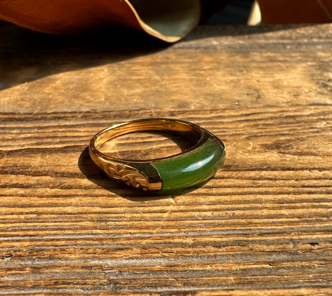 Gold ring featuring a green jade inlay and carved detail on a wooden surface